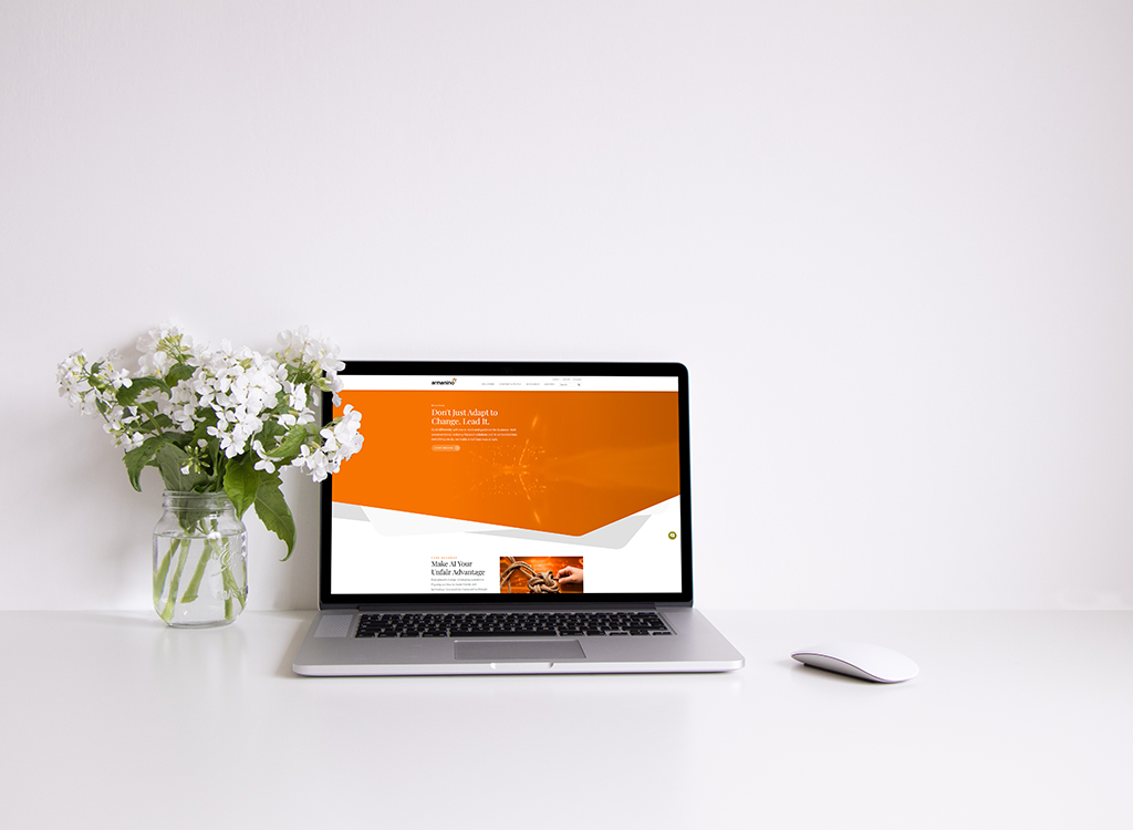 A modern workspace featuring a laptop displaying a vibrant website design with orange accents, alongside a glass vase of white flowers, creating an inviting and professional atmosphere.