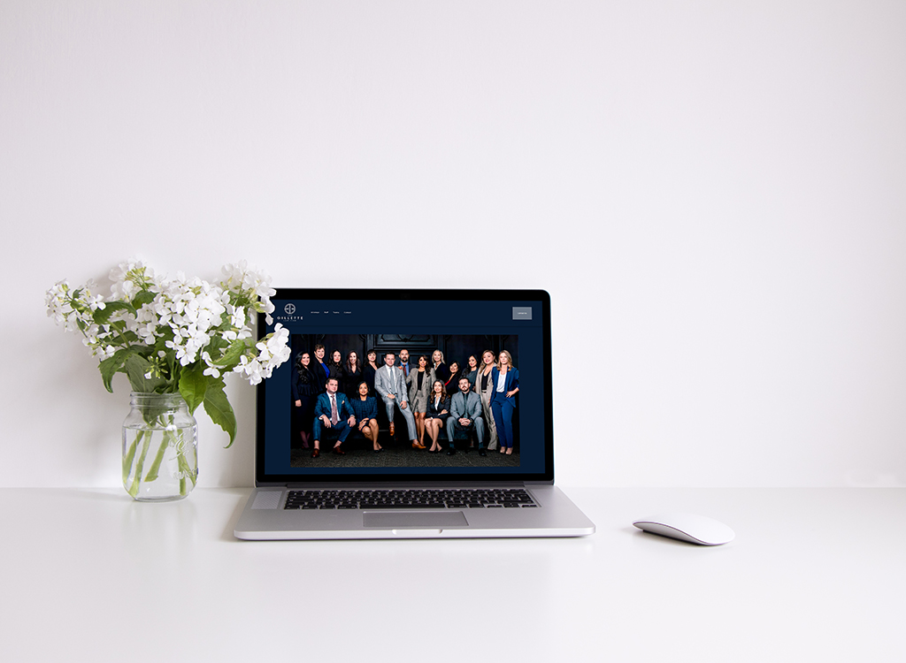 Laptop displaying a group photo of a professional team, with a vase of white flowers on a clean, minimalist desk.