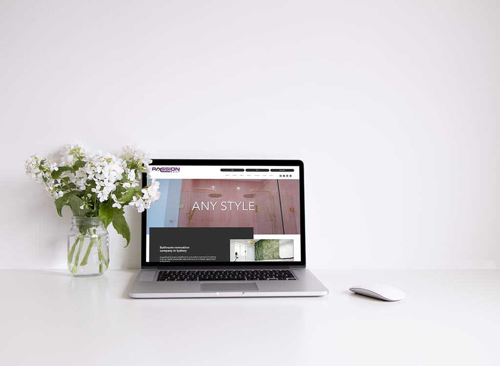 Laptop displaying a bathroom renovation website with the text "ANY STYLE" on the screen, accompanied by a vase of white flowers on a minimalistic desk.