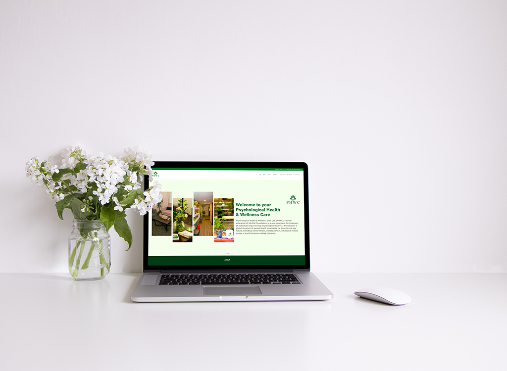 Laptop displaying a website for psychological health and wellness care, accompanied by a vase of white flowers on a minimalist desk.