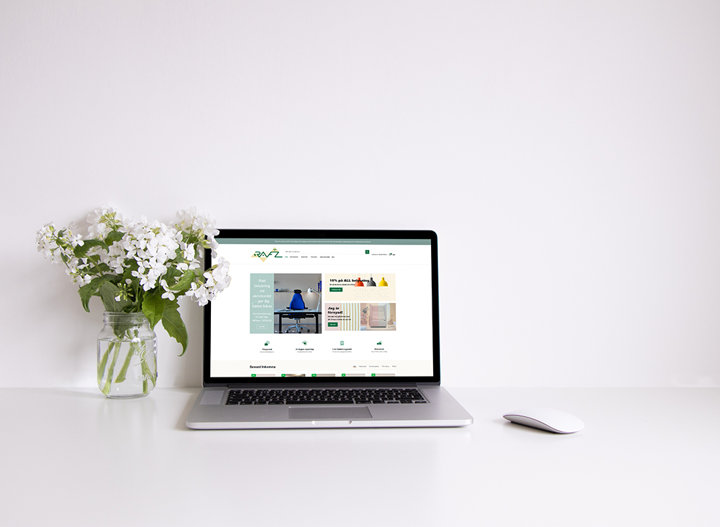 Laptop displaying a website on a minimalist desk with a mouse and a vase of white flowers, highlighting a clean, modern workspace.